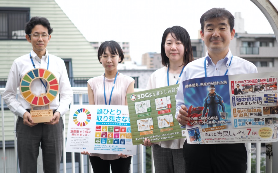 写真：SDGsのポスターやオブジェを掲げる担当職員たち