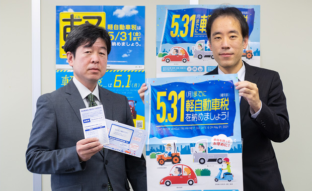 写真：担当者が軽自動車税納税のポスターや通知書を掲げている